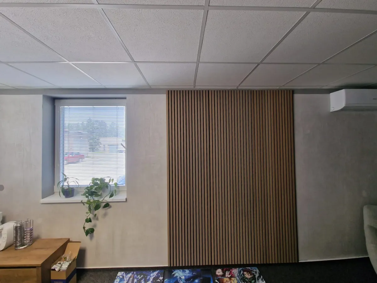 Stejná místnost jako kancelář, světle šedá stěrka na zdech, okno se žaluzií a&nbsp;dřevěné lamely
