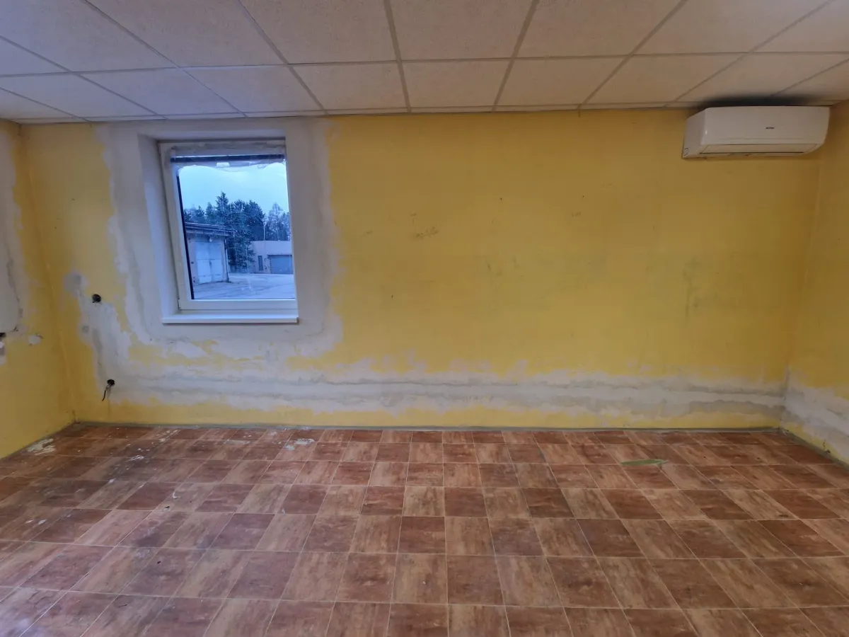 Místnost se žlutými zdmi, u&nbsp;podlahy a&nbsp;kolem okna otlučená omítka, na podlaze dlažba