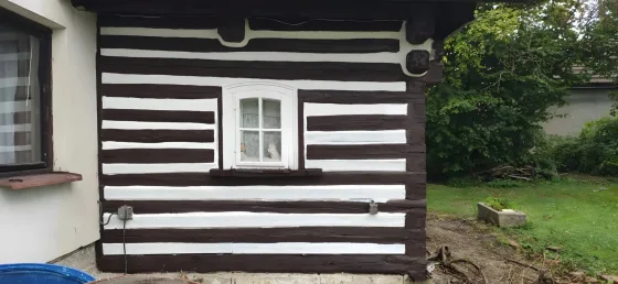 Stejná stěna po nátěru, tmavé trámy a&nbsp;čistě bílé spáry, bílé okno