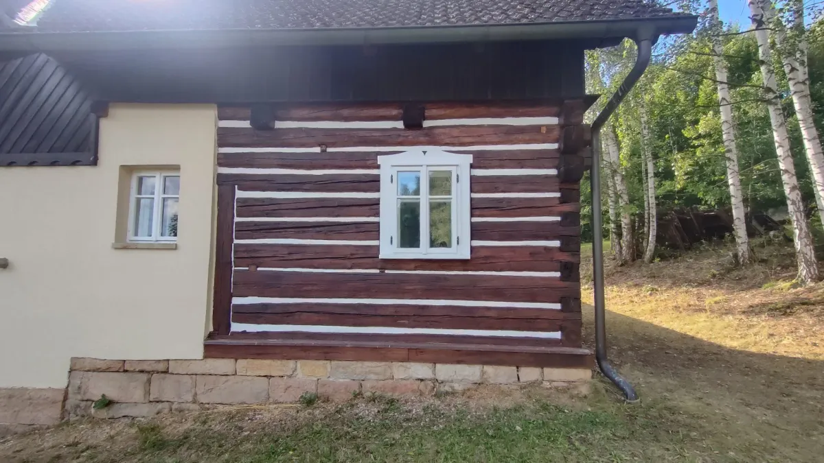 Stejná stěna po nátěru, tmavě hnědé trámy a&nbsp;bílé spáry kolem okna